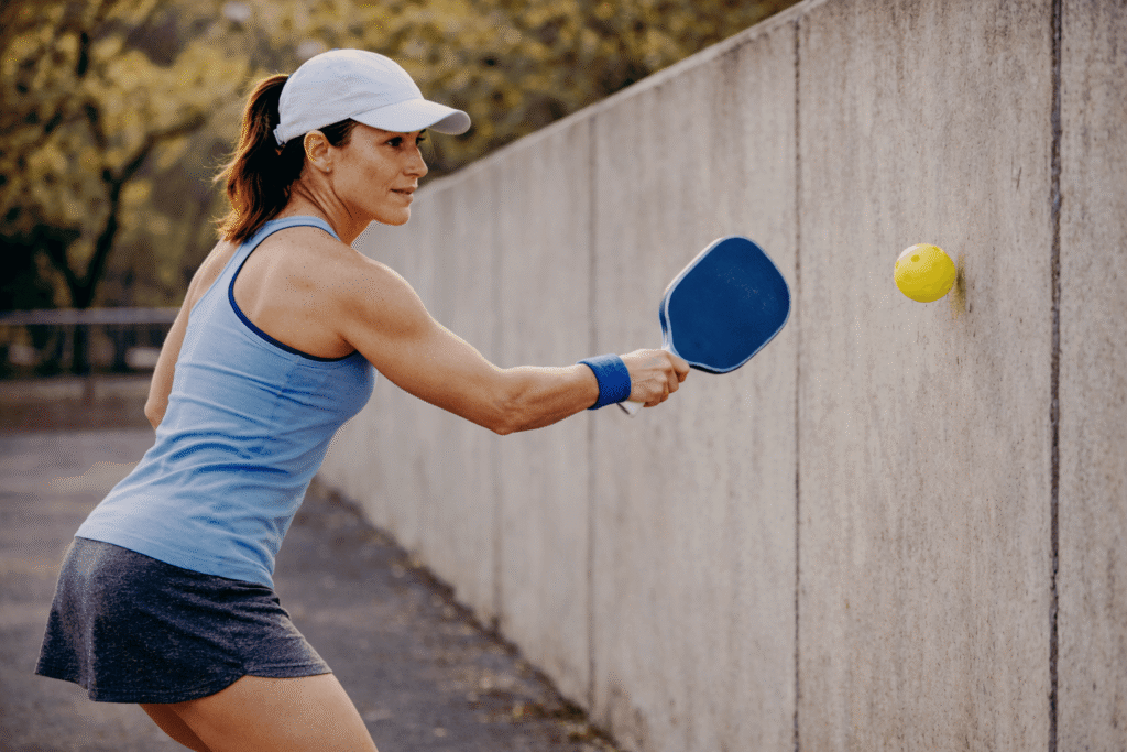 Female pickleball player practicing reset shot technique by hitting pickleball against a wall at close range