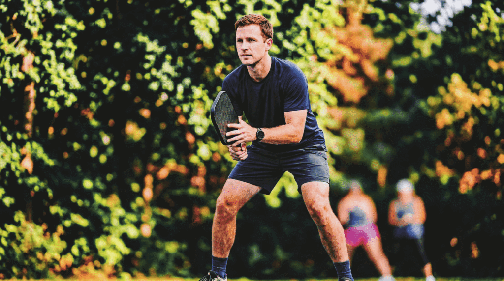 Male pickleball player in calm confident ready position at the kitchen line demonstrating the reliable steady presence of a good doubles partner.